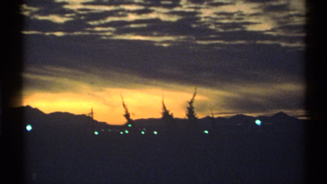 Dark mountain horizon and trees under a yellow-orange sunset with heavy clouds.