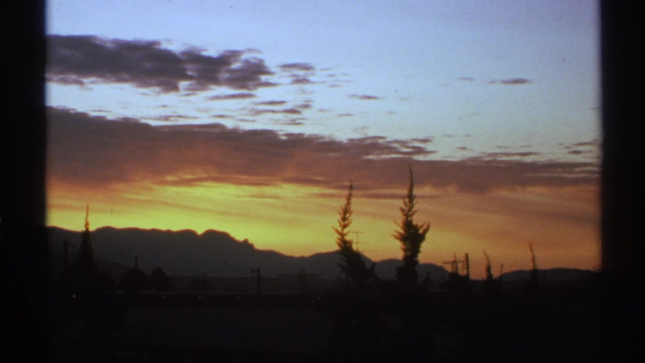 1972 Arizona 8mm frame showing a glowing desert sunset behind silhouetted mountains, trees, poles, and power lines.