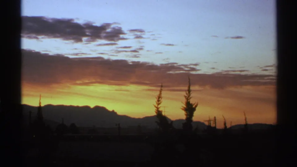 1972 Arizona 8mm frame showing a glowing desert sunset behind silhouetted mountains, trees, poles, and power lines.