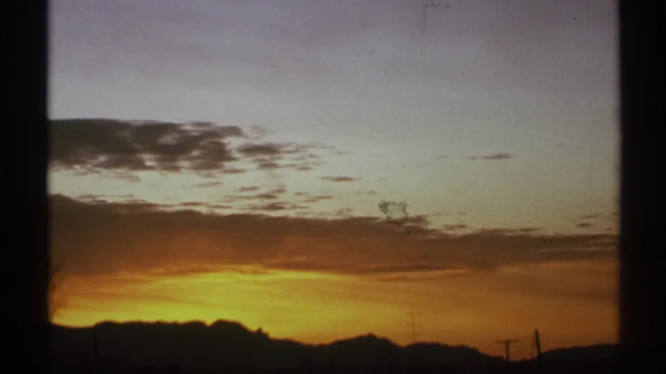 1972 Arizona 8mm frame showing a broad sunset cloud band over silhouetted desert mountains and faint utility lines.