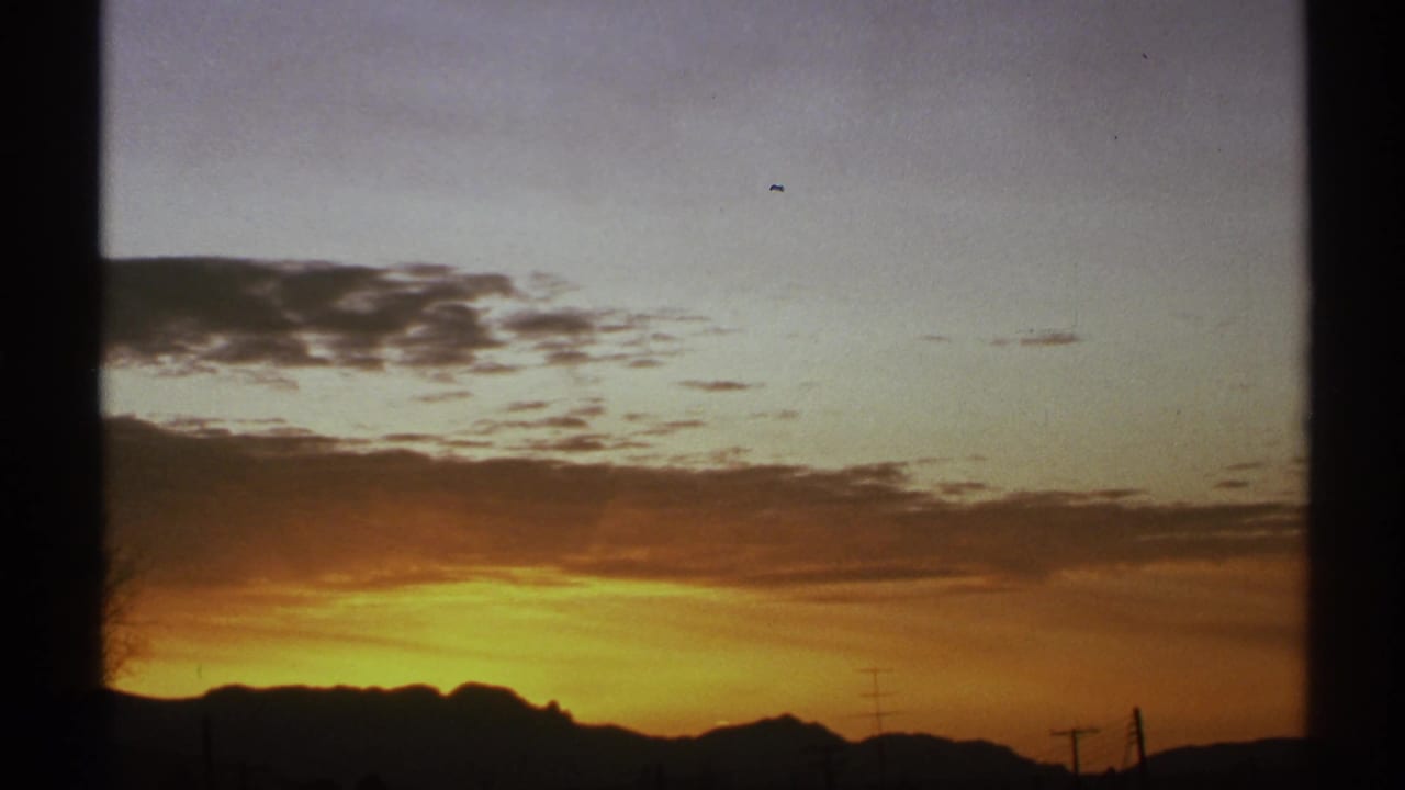 Sunset sky over a dark mountain ridgeline seen through a window frame.