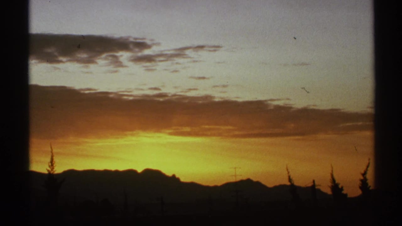 Bright sunset behind a dark mountain range with clouds and trees in silhouette.