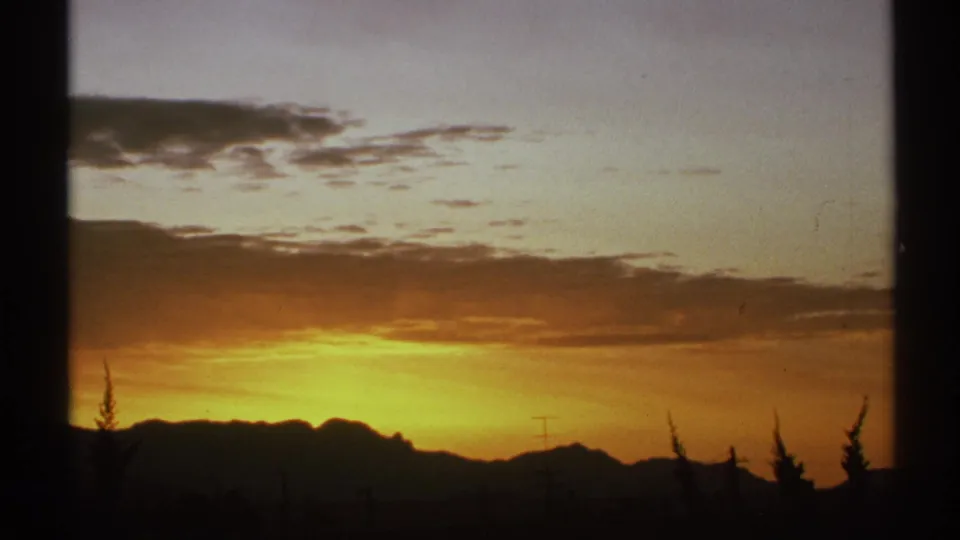 1972 Arizona 8mm frame showing a fading orange-purple sky, cloud layers, silhouetted desert mountains, utility poles, and trees.