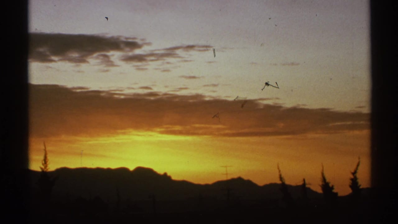 Orange sunset behind dark desert mountains, seen through a window-like frame.