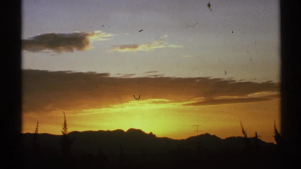 1972 Arizona frame with bright sunset color below cloud bands, dark mountains, and silhouetted desert plants.