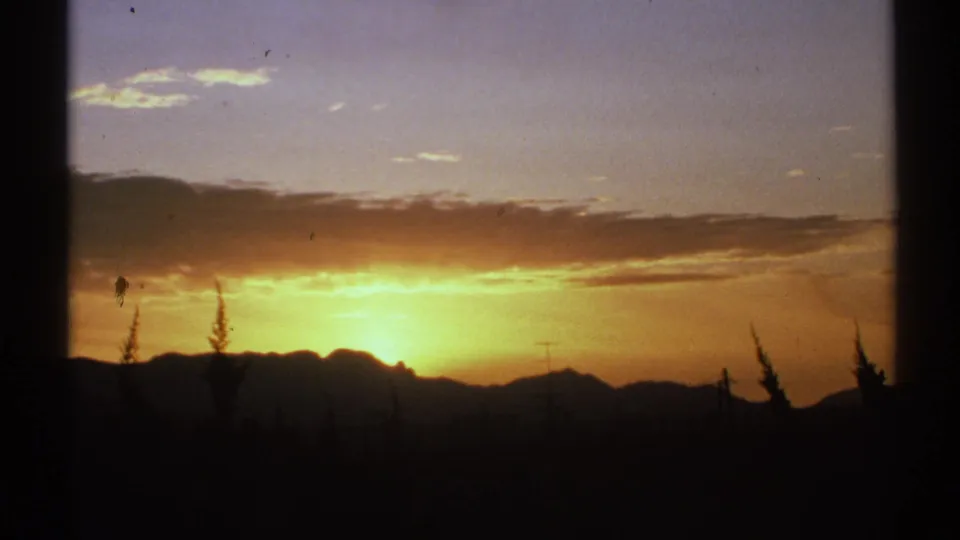 Arizona home-movie sunset frame showing glowing sky, distant mountain shapes, sparse vegetation, and film wear marks.
