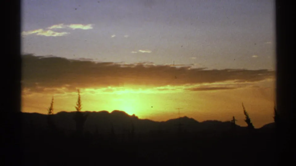 1972 Arizona 8mm frame with a fading orange sunset over silhouetted mountains, scattered clouds, and dark trees in the foreground.