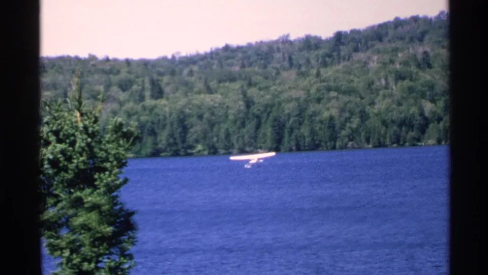The floatplane continues over Isle Royale lake water, framed by forested shoreline and dark scan borders.