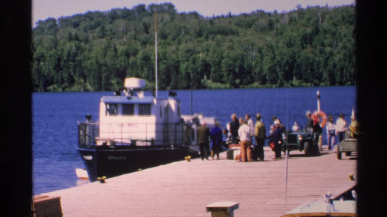 White mail boat at a lakeside dock with people waiting nearby.