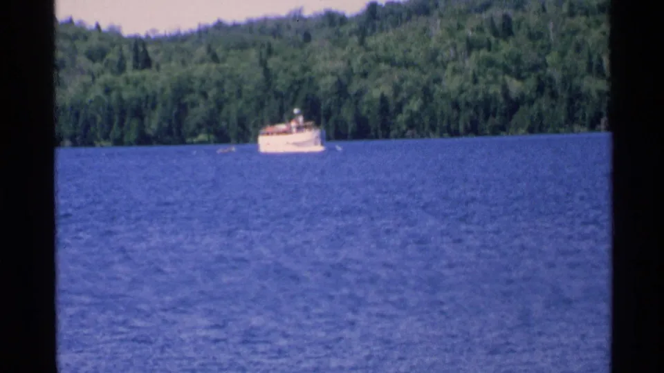 The white boat appears underway on Isle Royale waters, seen from a distance against a dense green shoreline.