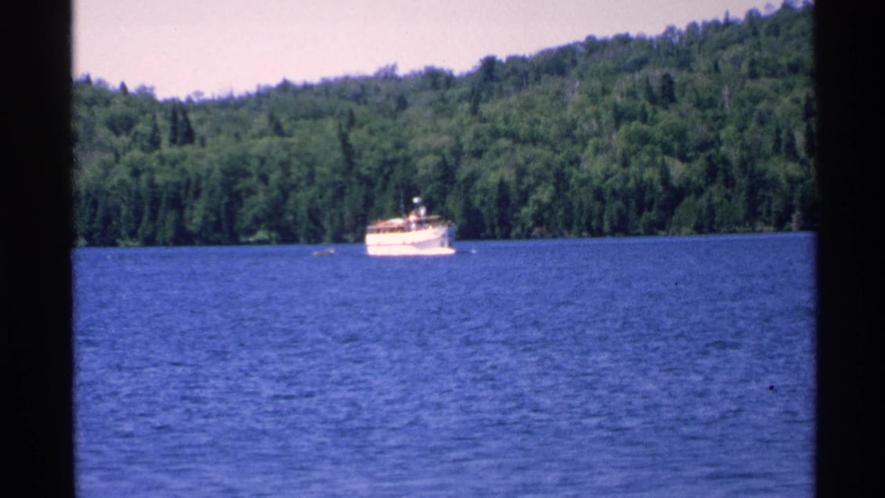 White boat on a blue lake with forested shoreline behind it.