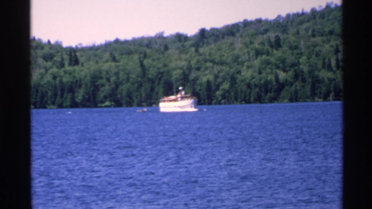 White boat farther across the lake with dense trees in the background.