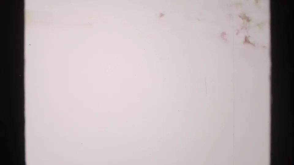 Blank 8mm leader frame with pale exposure, faint specks, and dark vertical film borders at the end of the clip.