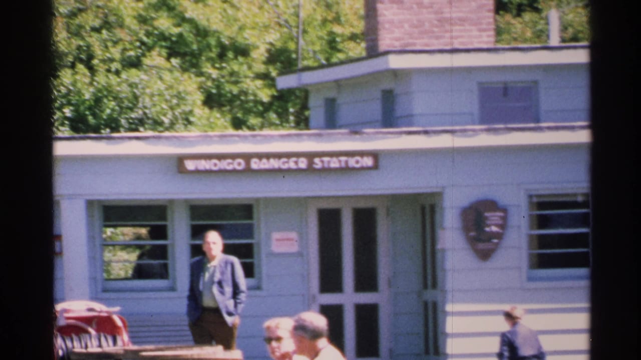 A visitor stands near the Windigo Ranger Station entrance on Isle Royale, with the sign and National Park Service shield visible.