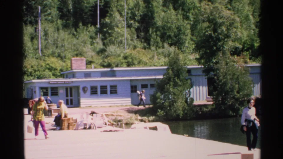 Wide Isle Royale view with Windigo Ranger Station in the background and visitors walking or sitting near the pier and lake.