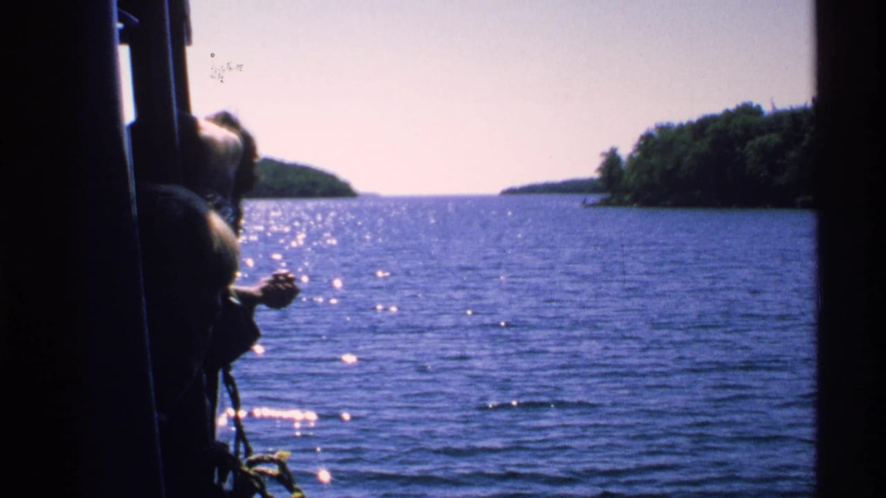 Isle Royale boat-travel view across sparkling blue water toward tree-lined islands, with dark boat framing at the edge.