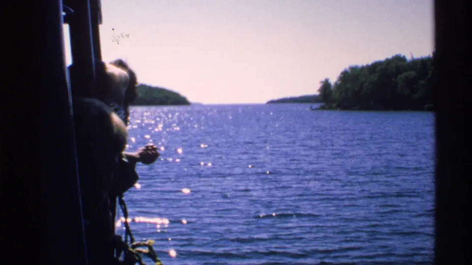 Isle Royale boat-travel view across sparkling blue water toward tree-lined islands, with dark boat framing at the edge.