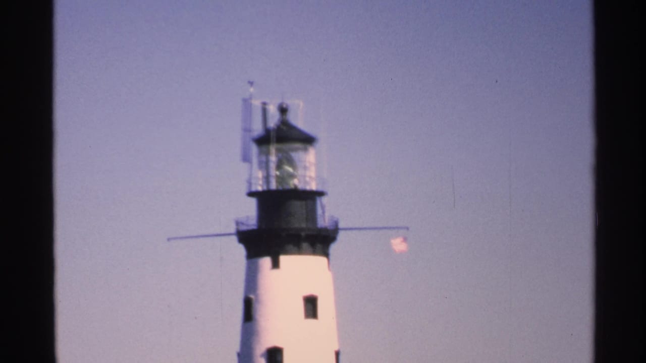 1972 Isle Royale footage frame with the lighthouse lantern room and flag seen through dark vertical frame edges.