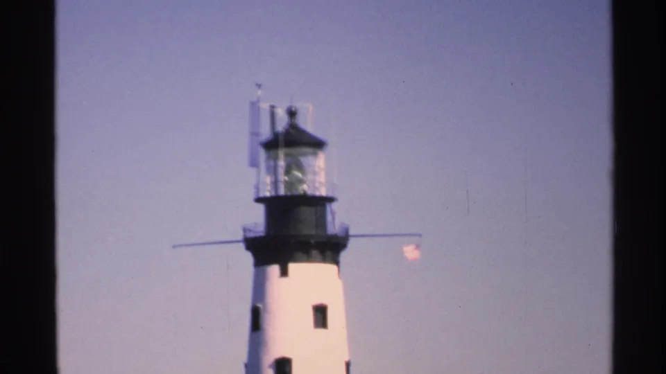 1972 Isle Royale footage frame with the lighthouse lantern room and flag seen through dark vertical frame edges.