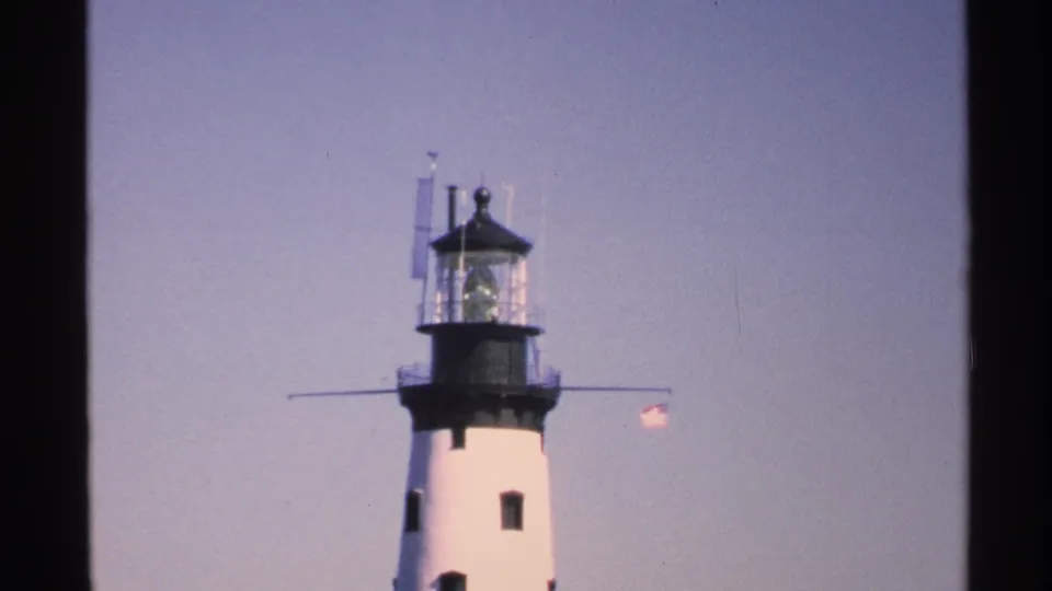1972 Isle Royale home-movie view of the lighthouse tower, dark lantern room, railings, and American flag.