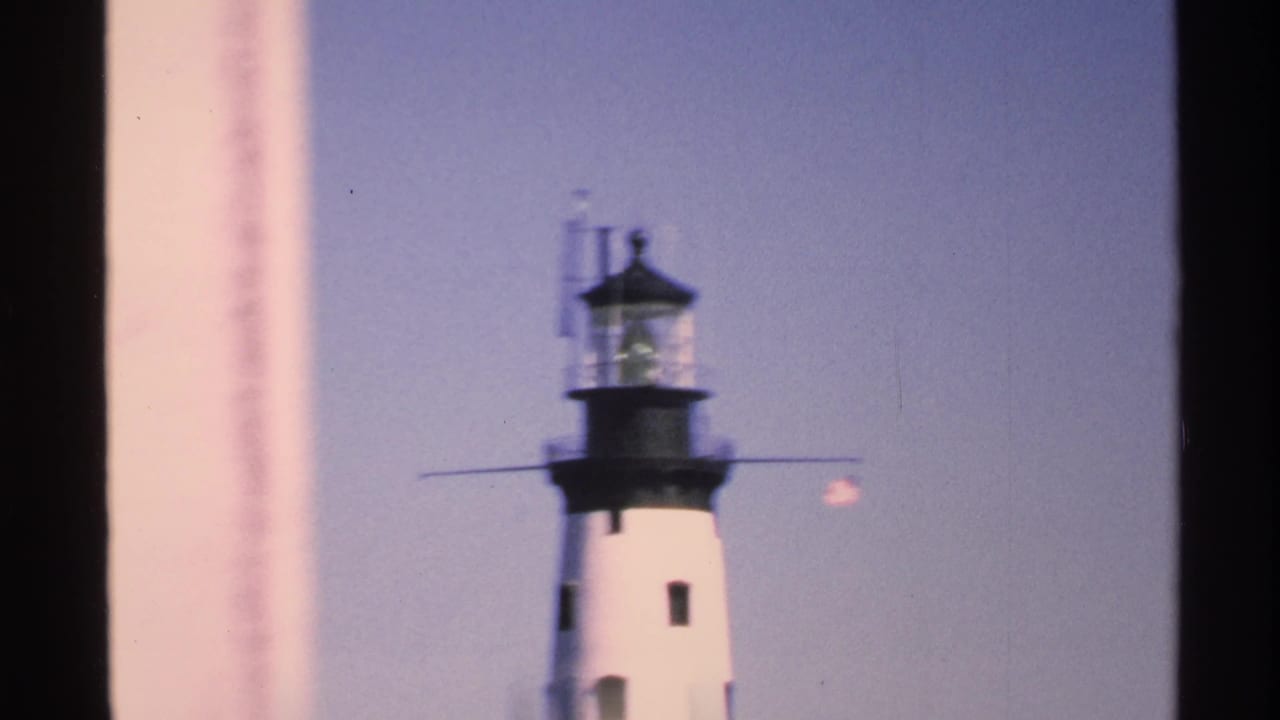Close view of a white lighthouse tower and black lantern room seen through dark vertical framing.