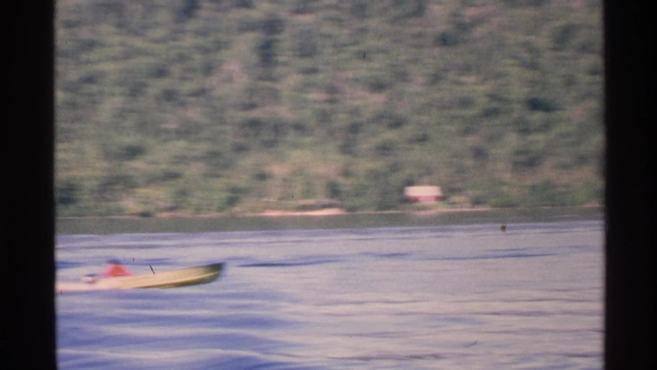 A distant small motorboat passes across Isle Royale lake water in a 1972 8mm home-movie view.