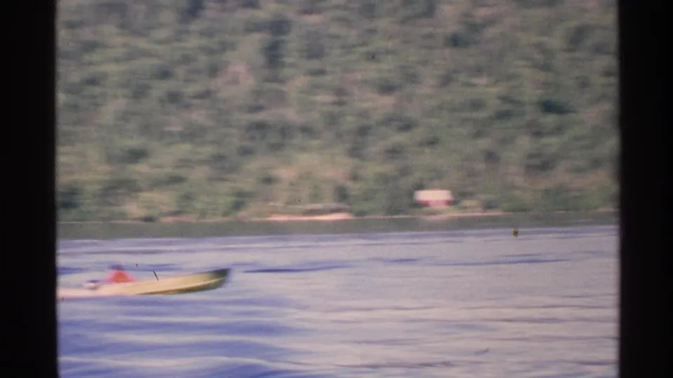 A distant small motorboat passes across Isle Royale lake water in a 1972 8mm home-movie view.