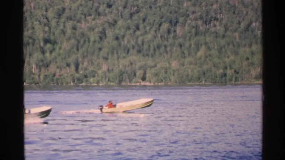 Two small boats appear on the lake near Isle Royale shoreline, one with a distant person in red aboard.