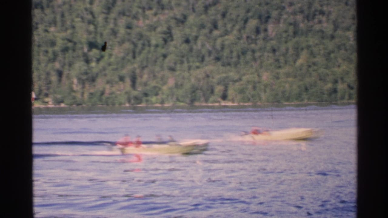 1972 Isle Royale home-movie frame showing two yellow speed boats crossing a calm lake before a wooded shoreline.