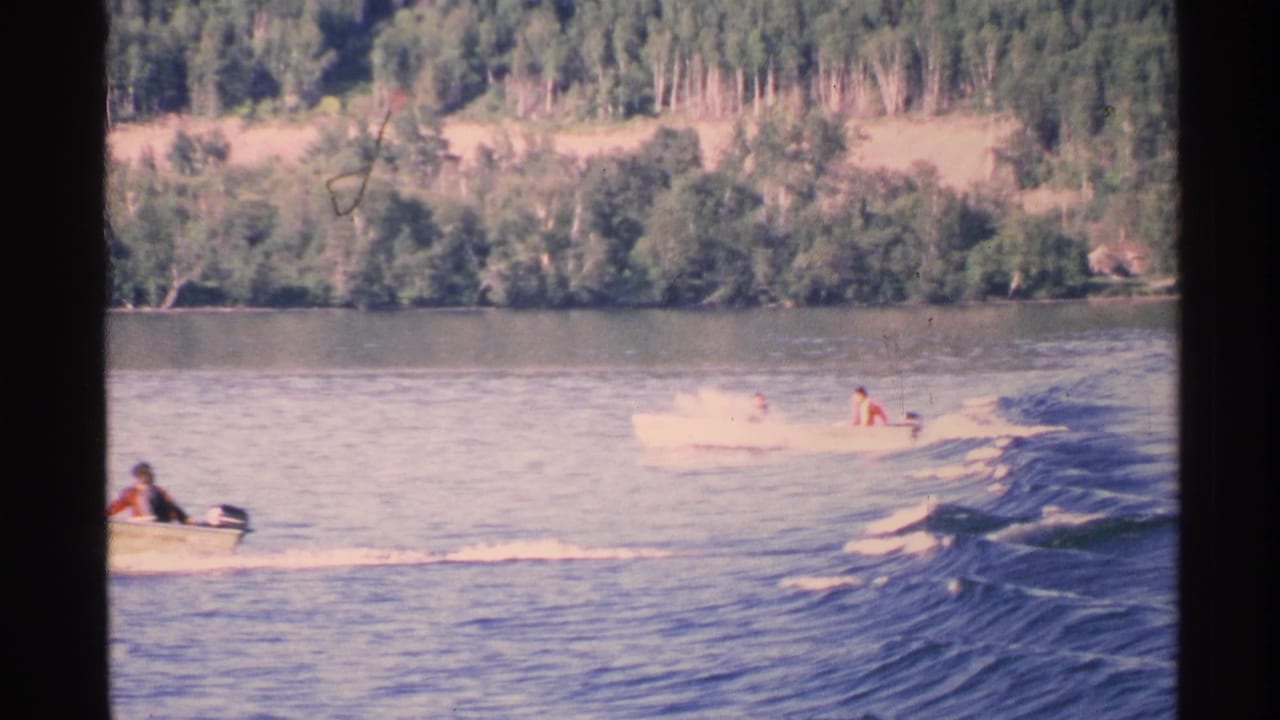 Two small motorboats move across rippled water near a wooded shoreline.
