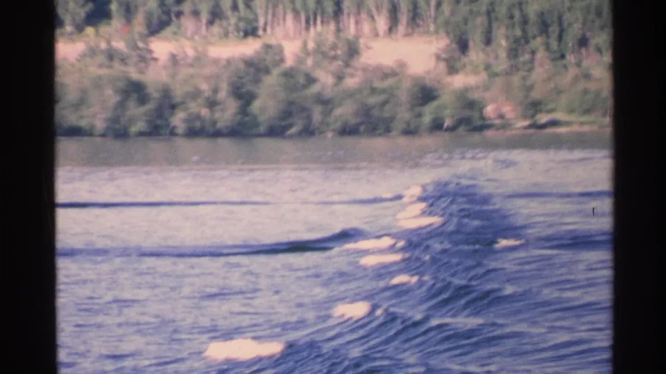A 1972 Isle Royale lake view with a long motorboat wake stretching across the water and dense trees in the background.