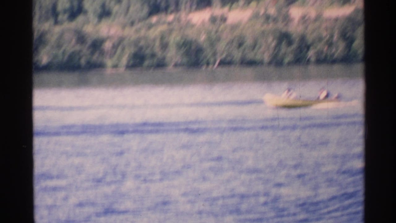 Small boat with two distant people on open lake water.