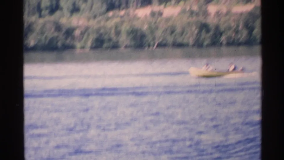 A small motorboat carrying two distant people glides across the lake in 1972 Isle Royale home-movie footage.