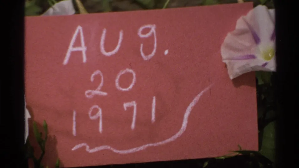 The red paper date card fills more of the 8mm frame, with white writing and a tucked flower at the side.