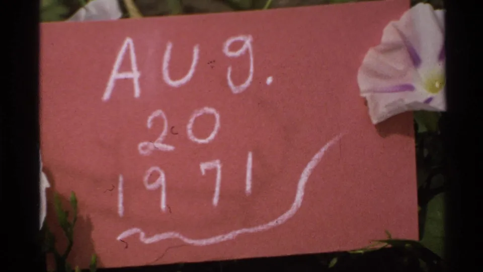 A soft 8mm frame shows the red handwritten date card and pale flower, marking Aug. 20, 1971 within the Isle Royale clip.