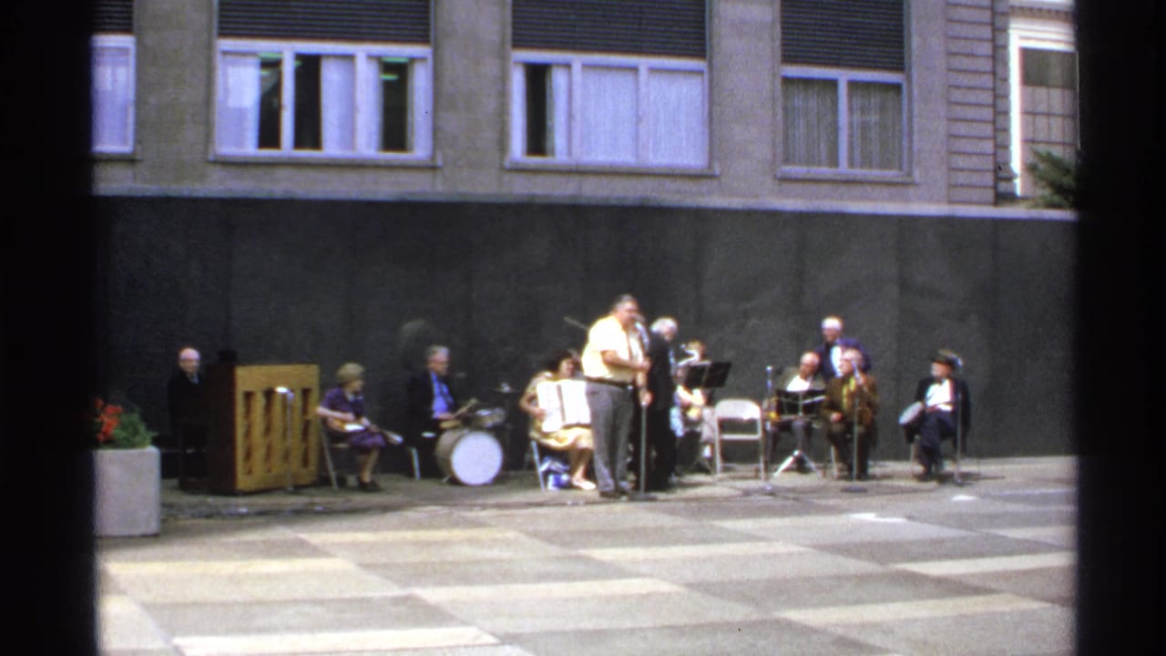 Small outdoor band performs in a paved courtyard against a building wall.