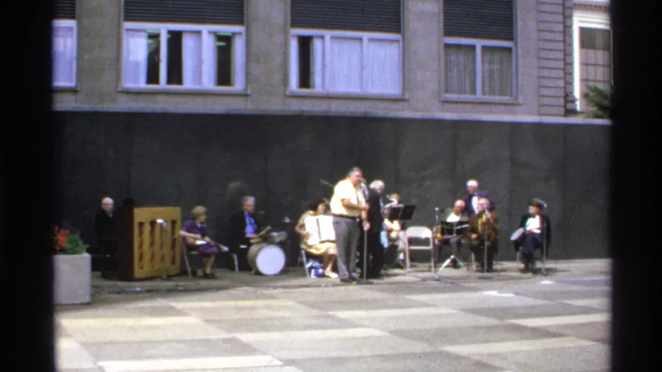 1972 Isle Royale home-movie frame showing adult musicians and a vocalist performing in a courtyard.