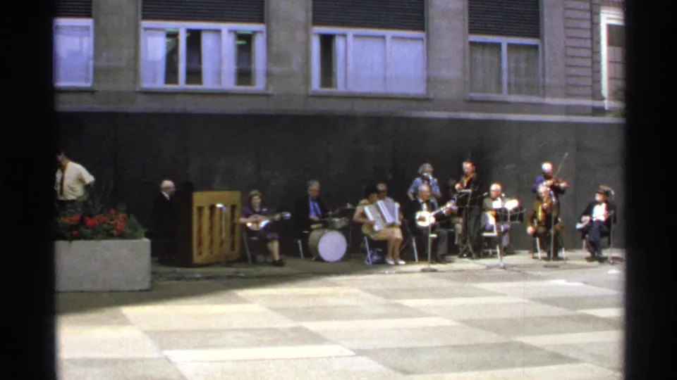 1972 Isle Royale home-movie frame of seated musicians, accordion, drum kit, and courtyard planter.
