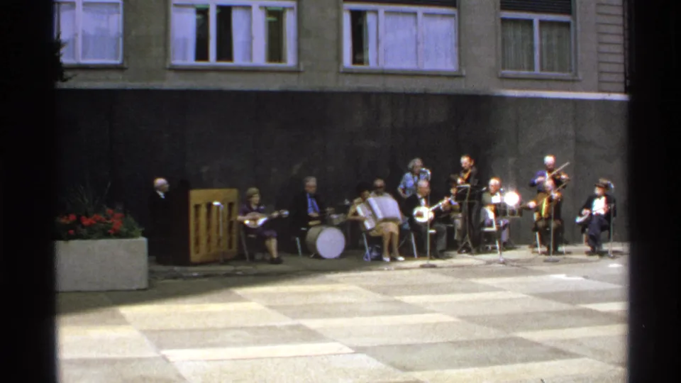 1972 Isle Royale home-movie frame showing a small outdoor ensemble performing against a building wall and windows.