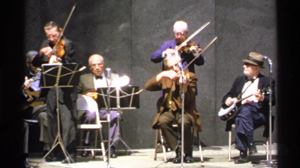 1972 Isle Royale frame showing violinists and a banjo player on a modest stage, with music stands and microphones visible.