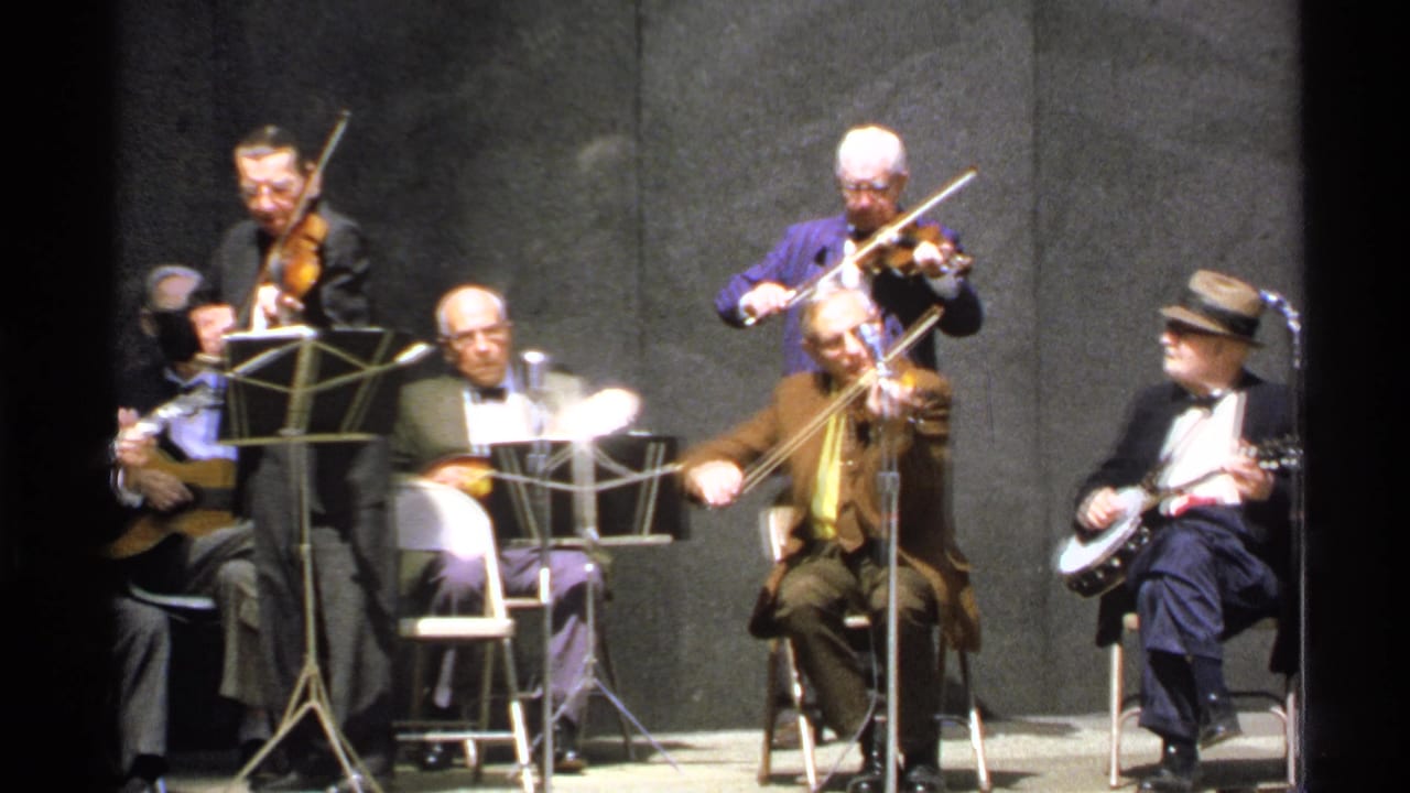 1972 Isle Royale footage shows older men in suits playing violins and banjo on stage with music stands and microphones.