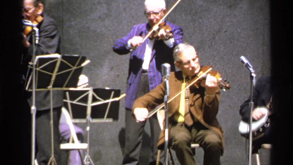 The final frame holds on the seated violinist playing on the Isle Royale stage, with a standing violinist and partial banjo player nearby.