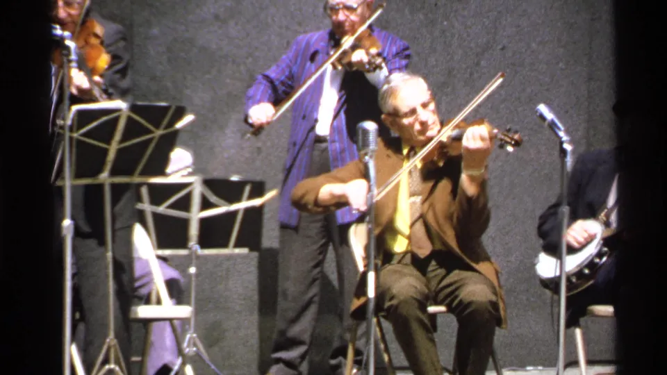 1972 Isle Royale stage performance with a seated violinist in front, other string players behind, and a banjo player partly visible.