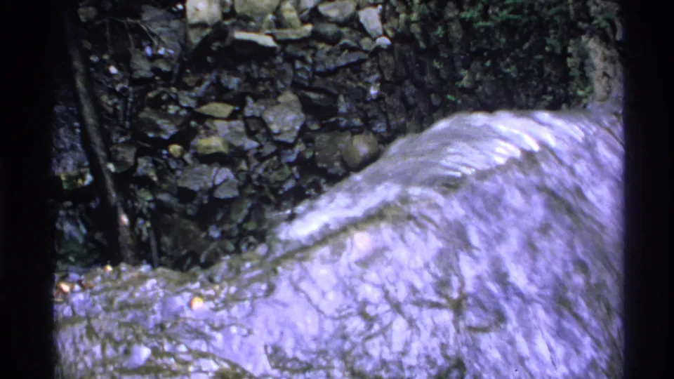 Close 1972 Isle Royale 8mm frame of water rushing over a pale rock surface beside dark ravine stones.