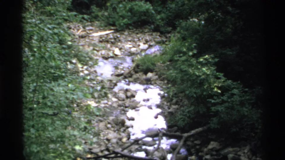 1972 Isle Royale frame showing white water in a rocky creek channel surrounded by dark green forest growth.