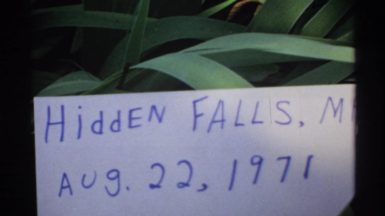 Handwritten Hidden Falls sign held near green leaves.