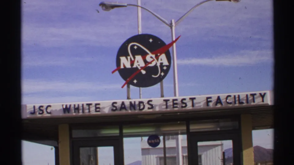 1972 New Mexico 8mm frame with a closer visitor view of the NASA logo, facility name, glass doors, and building facade.