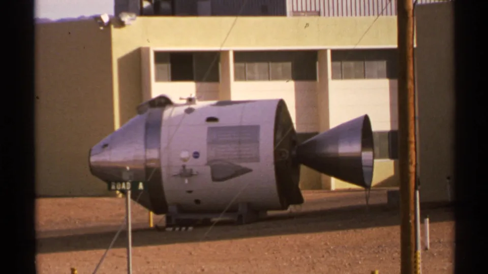 Closer 1972 New Mexico 8mm view of a silver spacecraft capsule-like exhibit standing outside the yellow building.