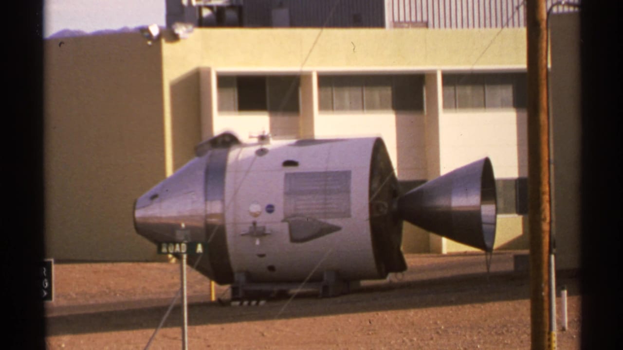 Silver command-module-like capsule displayed outside a beige building.