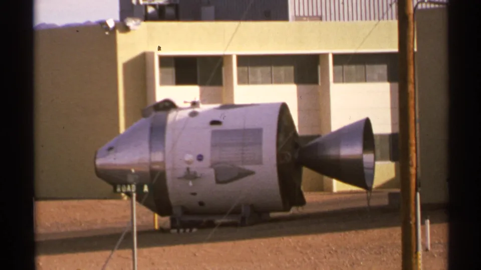 1972 New Mexico home-movie view of a silver command-module-like display with a conical rear section near a beige building.